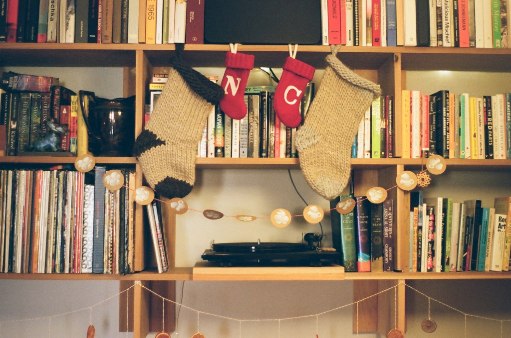 A full bookshelf with four stockings and a paper popcorn garland.