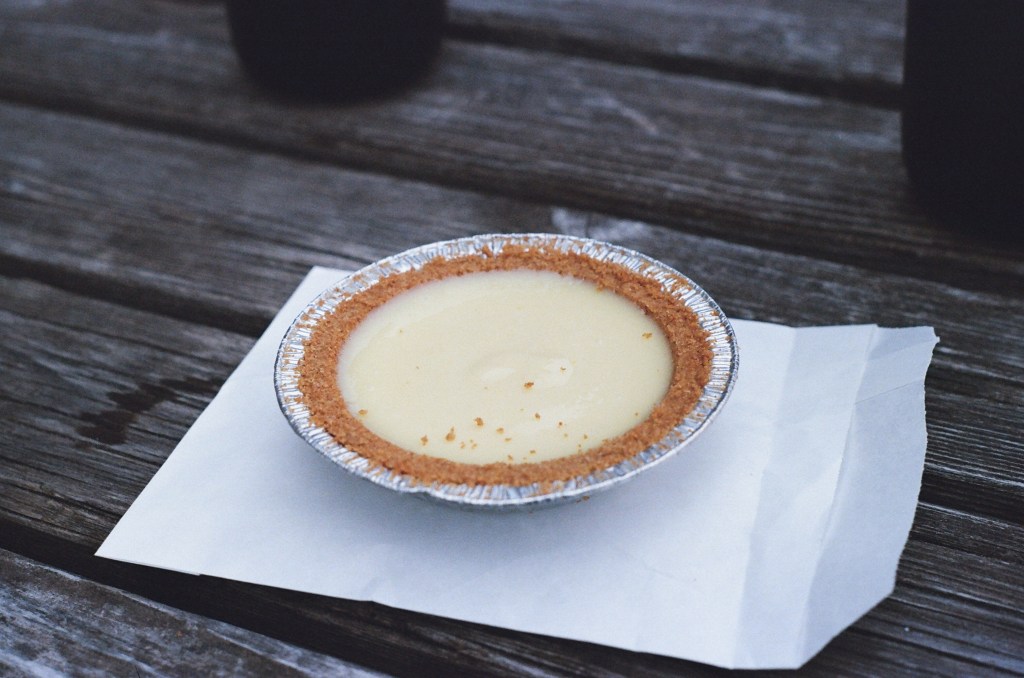 miniature key lime pie, sitting on a white paper back on a gray wood picnic table top