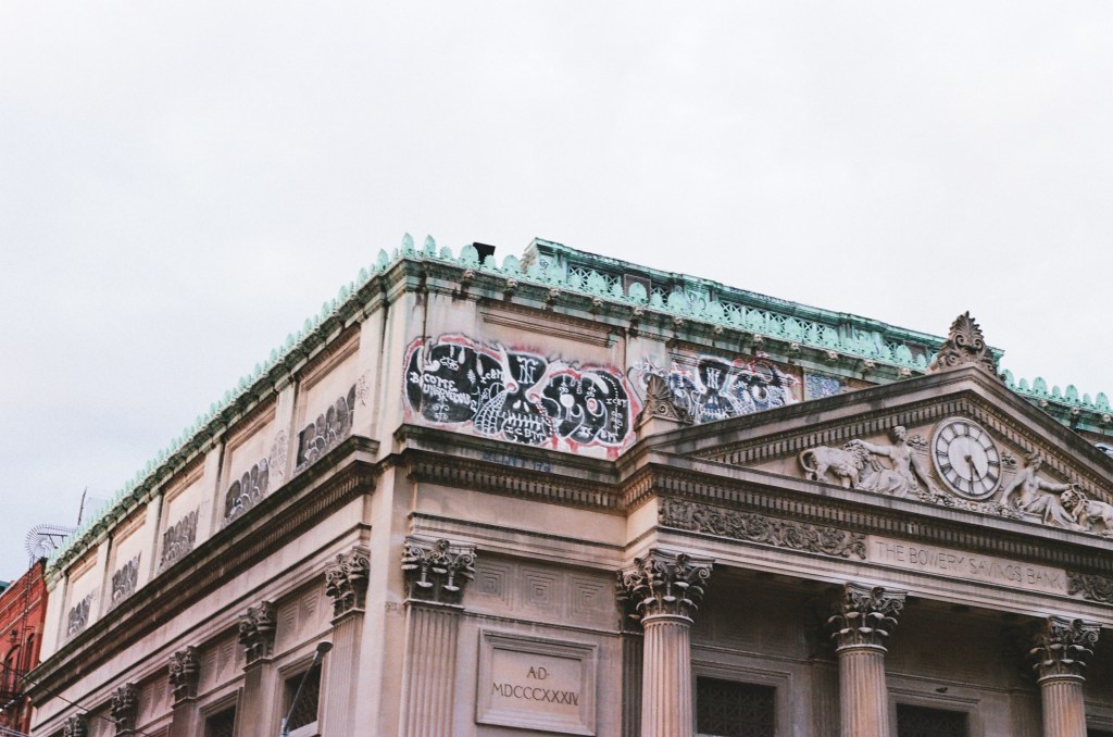 the top half of of the Bowery Savings Bank, a neoclassical building with symmetric graffiti across the top
