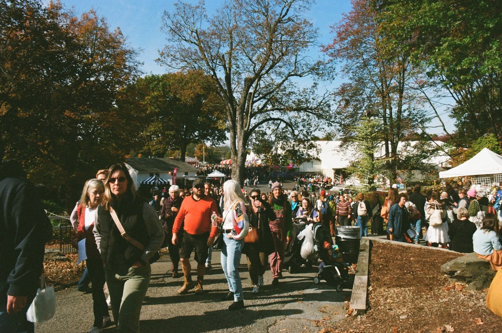 A crowd of people coming up a paved hill at what appears to be an outdoor event or convention. (It's the New York Sheep and Wool Festival in Rhinebeck, NY.)