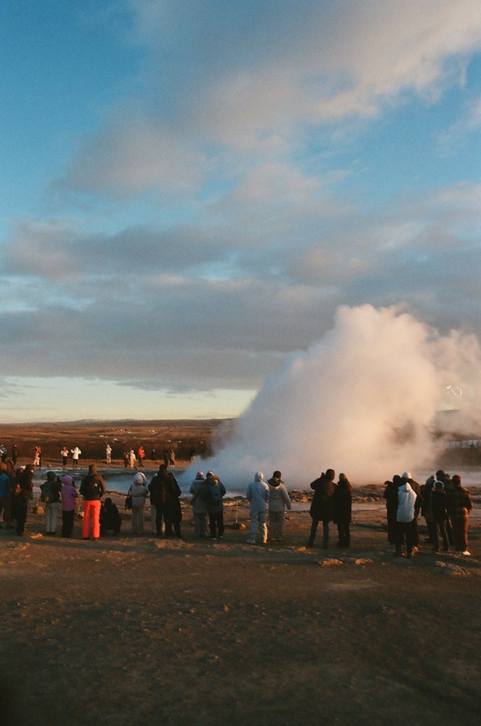Immediately following the eruption of a geyser, a cloud of steam lingers in the air before onlookers.