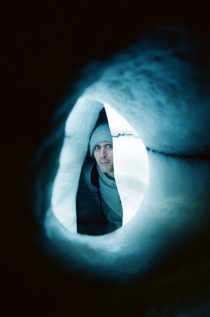 A white man in his mid-30s makes a silly face, peering through a hole in a man-made ice cave at the Perlan Natural History Museum in Reykjavik.