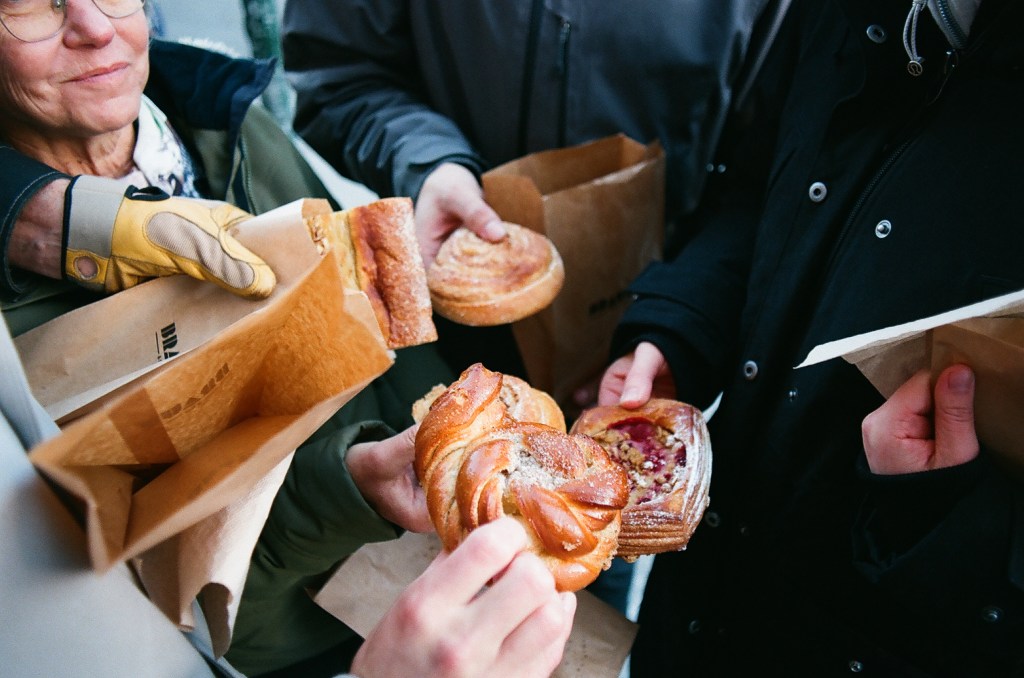 A group of people hold pastries out to the center of the group.