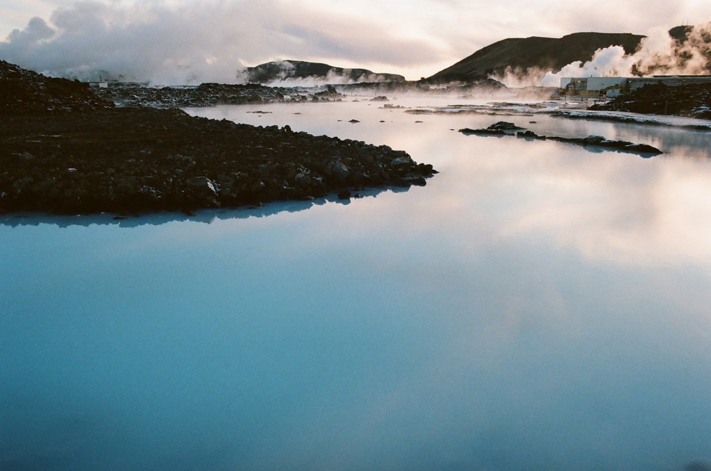The Blue Lagoon in Iceland, with calm, cloudy blue water nestled among dark volcanic rock.