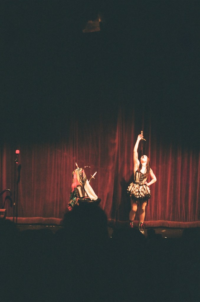 A grainy photo of a sword swallower in front of a red velvet background.
