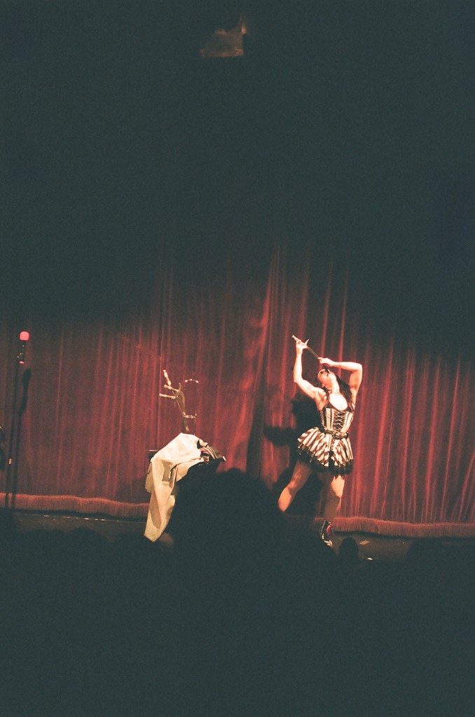 A grainy photo of a sword swallower in front of a red velvet background.