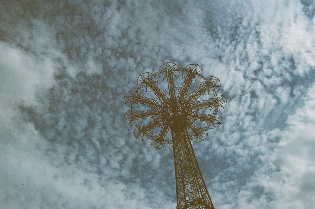 Looking up at the parachute jump at Coney Island, with small clouds all across the sky.